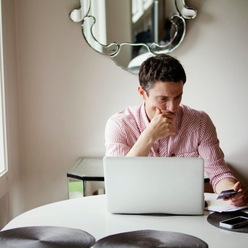 man-looking-at-credit-card-while-siting-by-table-1.jpg